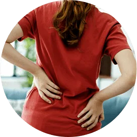 Εικόνα μιας γυναίκας από πίσω, που φοράει κόκκινο μπλουζάκι, με στάση πόνου ή δυσφορίας στο κάτω μέρος της πλάτης, που υποδηλώνει πιθανό πρόβλημα στην πλάτη.
