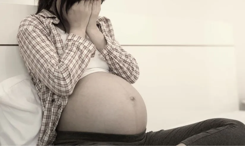 Sarah, pregnant, sitting on her bed holding her lower back in pain.